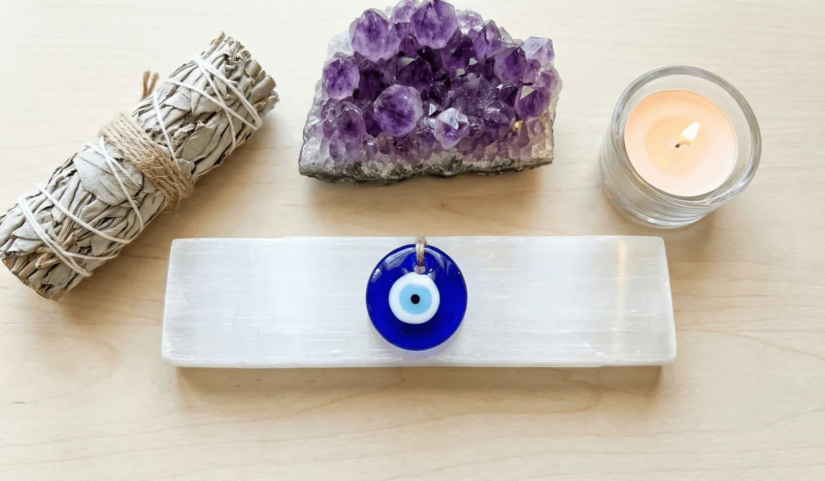 The Meaning of the Evil Eye: A Guide to Protection and Spiritual Symbolism 4 - Buddha Bodhis A spiritual cleansing setup featuring an Evil Eye necklace on a selenite plate with sage and crystals for energy charging.