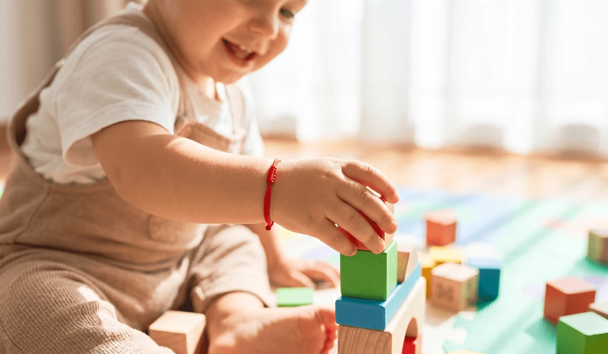 Red String Bracelets for Children: Meaning, Safety, and Traditions of Protection 2 - Buddha Bodhis A toddler playing safely while wearing a red string protection bracelet on the left wrist.