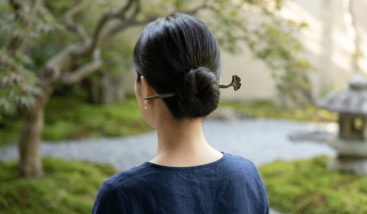 The Art of Mindful Styling: Elegant Hairstyles Using a Single Hair Stick - Buddha Bodhis A minimalist Zen hair bun secured with a single sandalwood hair stick in a serene garden setting.
