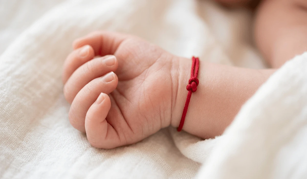 Red String Bracelets for Babies: Understanding the Tradition and Safety Guidelines - Buddha Bodhis Close-up of a newborn baby's hand wearing a safe, thin red silk string bracelet for spiritual protection.