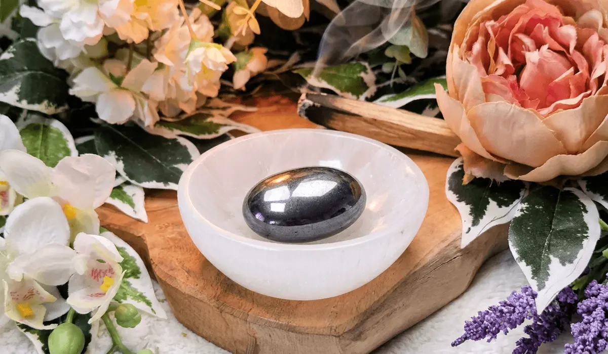 How to Tell If Hematite Is Real: Magnetism, Tests, and Authenticity 4 - Buddha Bodhis Smooth dark hematite palm stone resting inside a white translucent selenite bowl for energetic charging and dry cleansing.