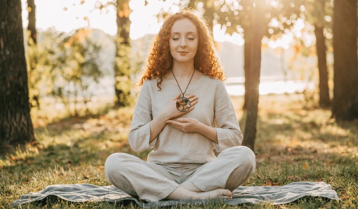 The 7 Chakra Tree of Life Pendant: Meaning, Symbolism, and Spiritual Balance 4 - Buddha Bodhis Woman meditating outdoors in nature wearing a 7 Chakra Tree of Life necklace resting near her heart center.