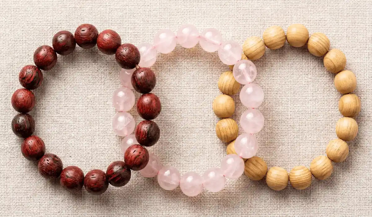 Which Hand Should You Wear a Rosewood Bracelet On? (Left vs. Right Wrist) 3 - Buddha Bodhis Comparison flatlay image displaying a dark rosewood bracelet, a pink rose quartz bracelet, and a light sandalwood bracelet side by side on linen.